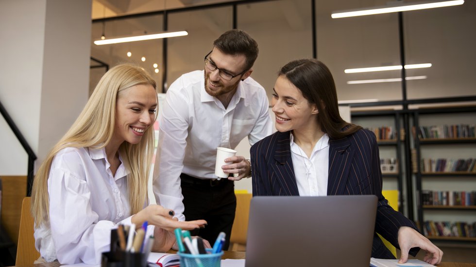 3 pracownicy w biurze rozmawiają przy laptopie